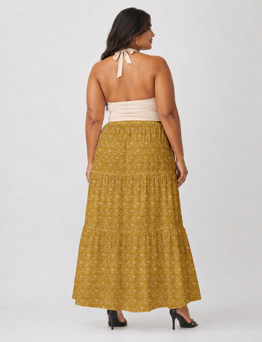 Woman wearing a yellow midi tiered skirt with a small geometric pattern, paired with a beige strapless top and white heels