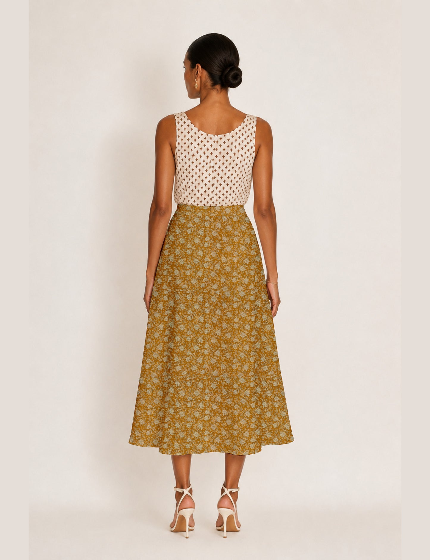 Woman wearing a yellow and black micro patterned A-line skirt with front slit, paired with beige sleeveless top and black