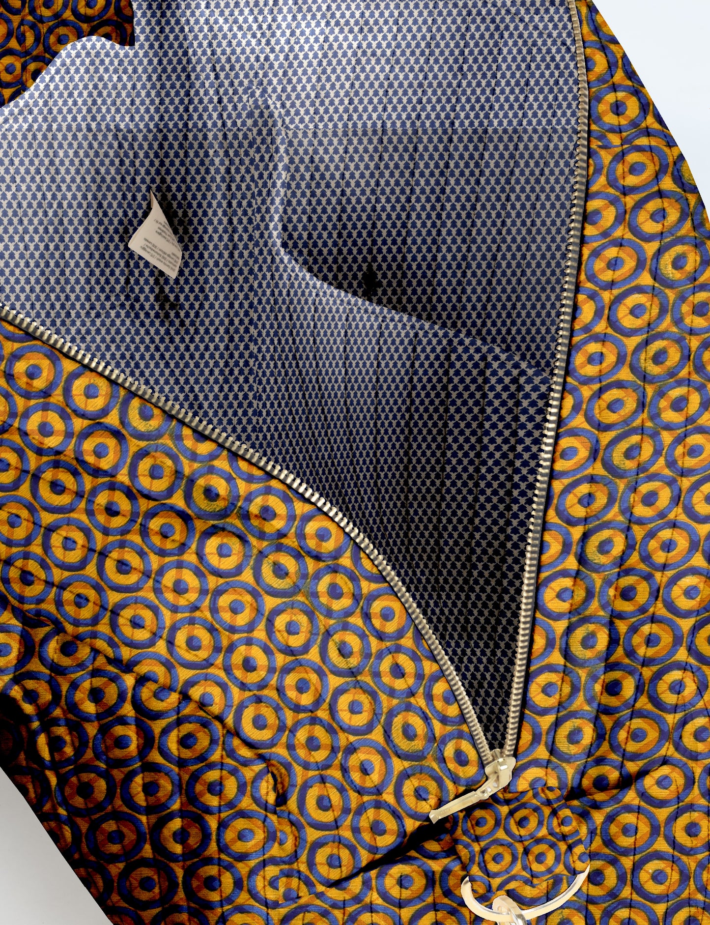Quilted duffle bag with yellow and blue circular geometric pattern, silver zipper, and blue patterned interior lining