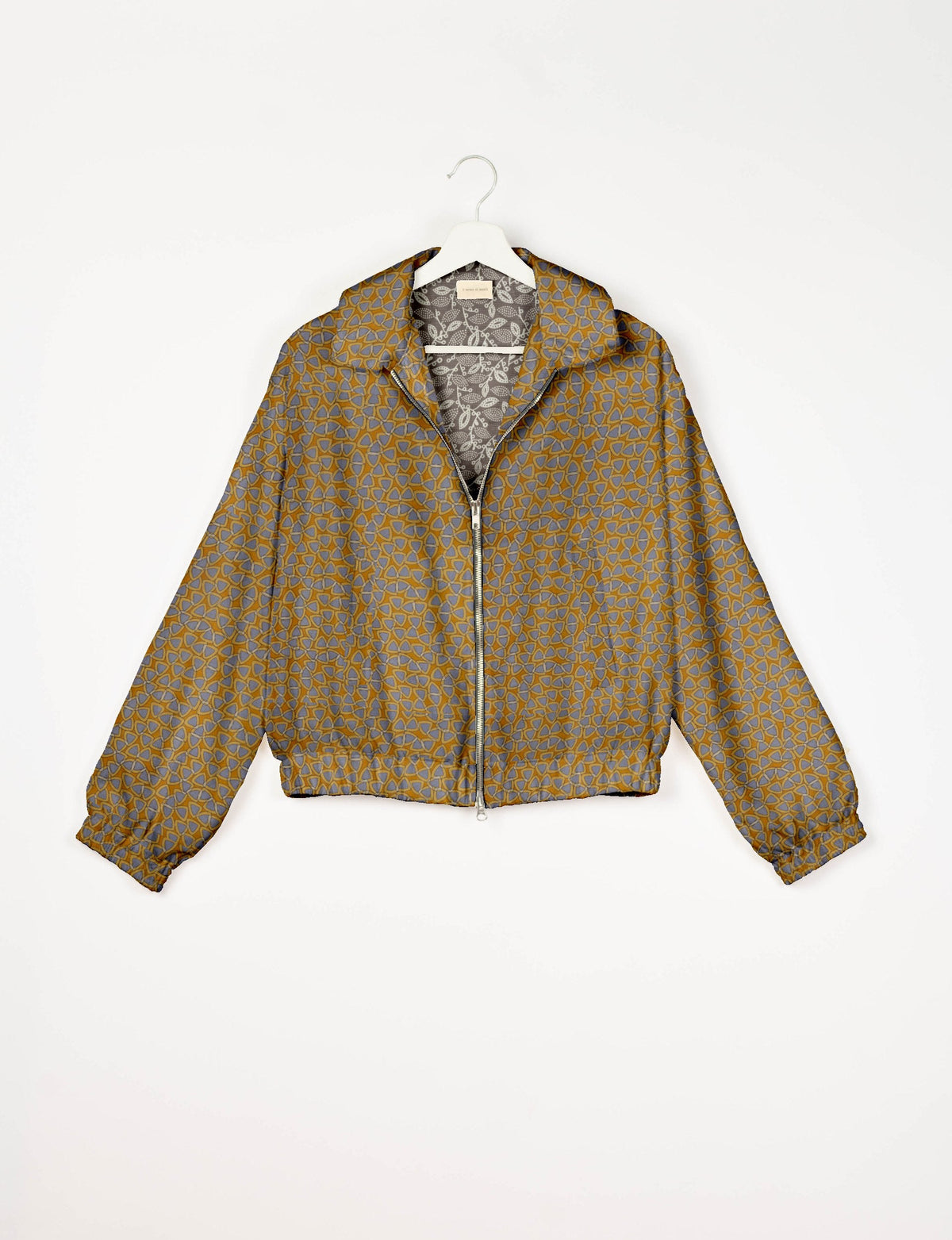Yellow and gray geometric patterned bomber jacket with front zipper, collar, and elastic cuffs, hanging on white hanger