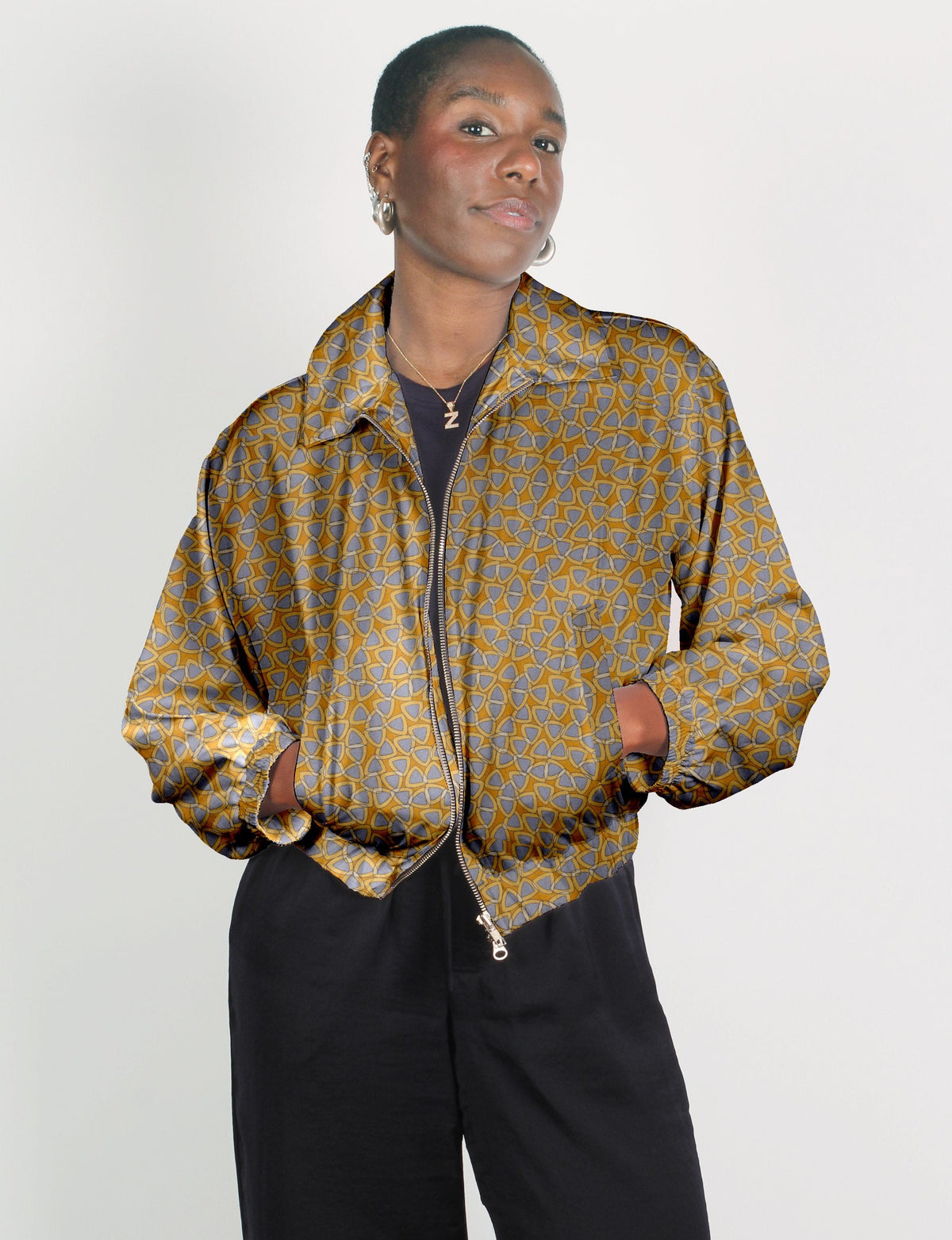 Woman wearing a yellow bomber jacket with a blue geometric pattern, front zipper, elastic cuffs, and black pants, front view