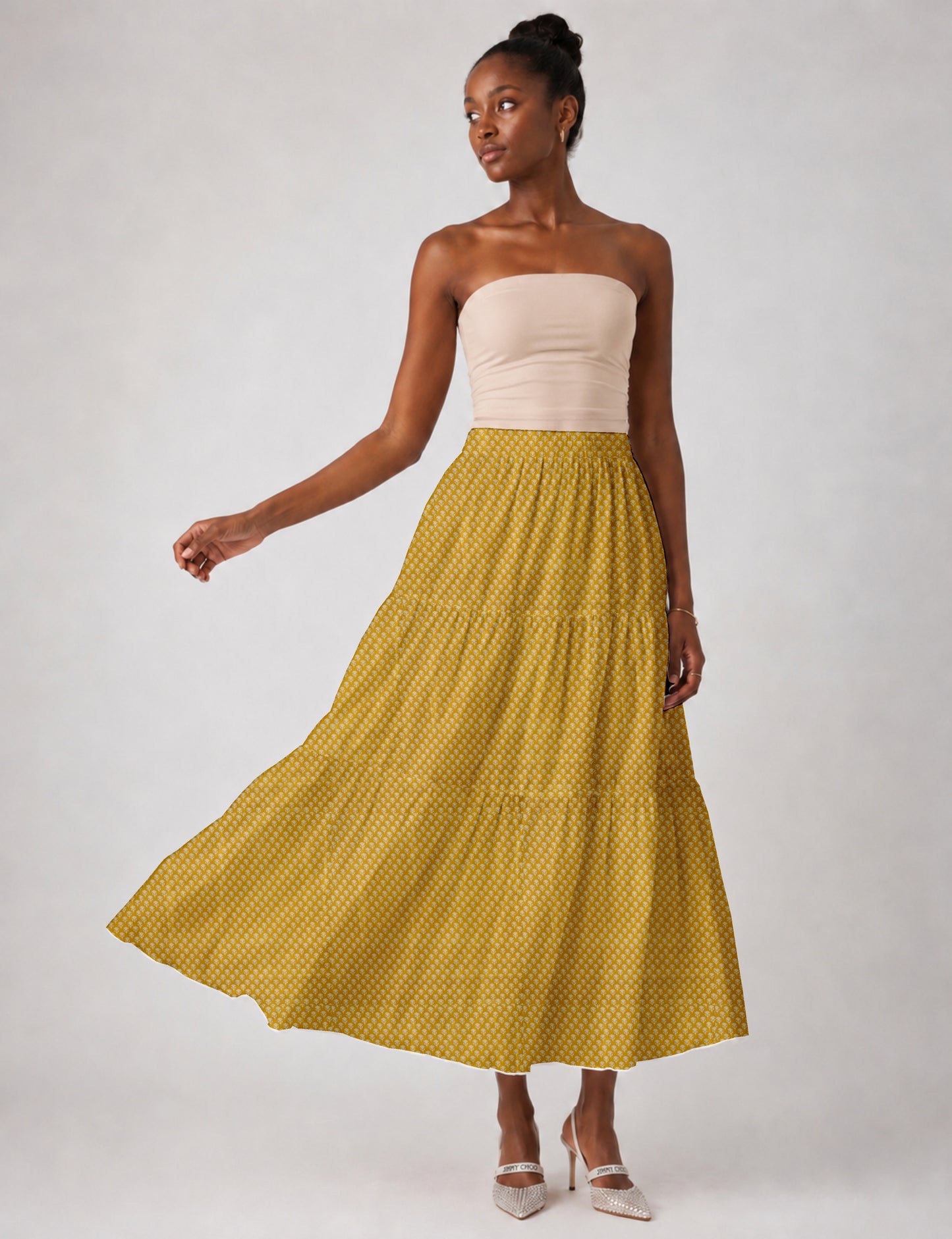 Woman wearing a yellow midi tiered skirt with a small geometric pattern, paired with a beige strapless top and white heels