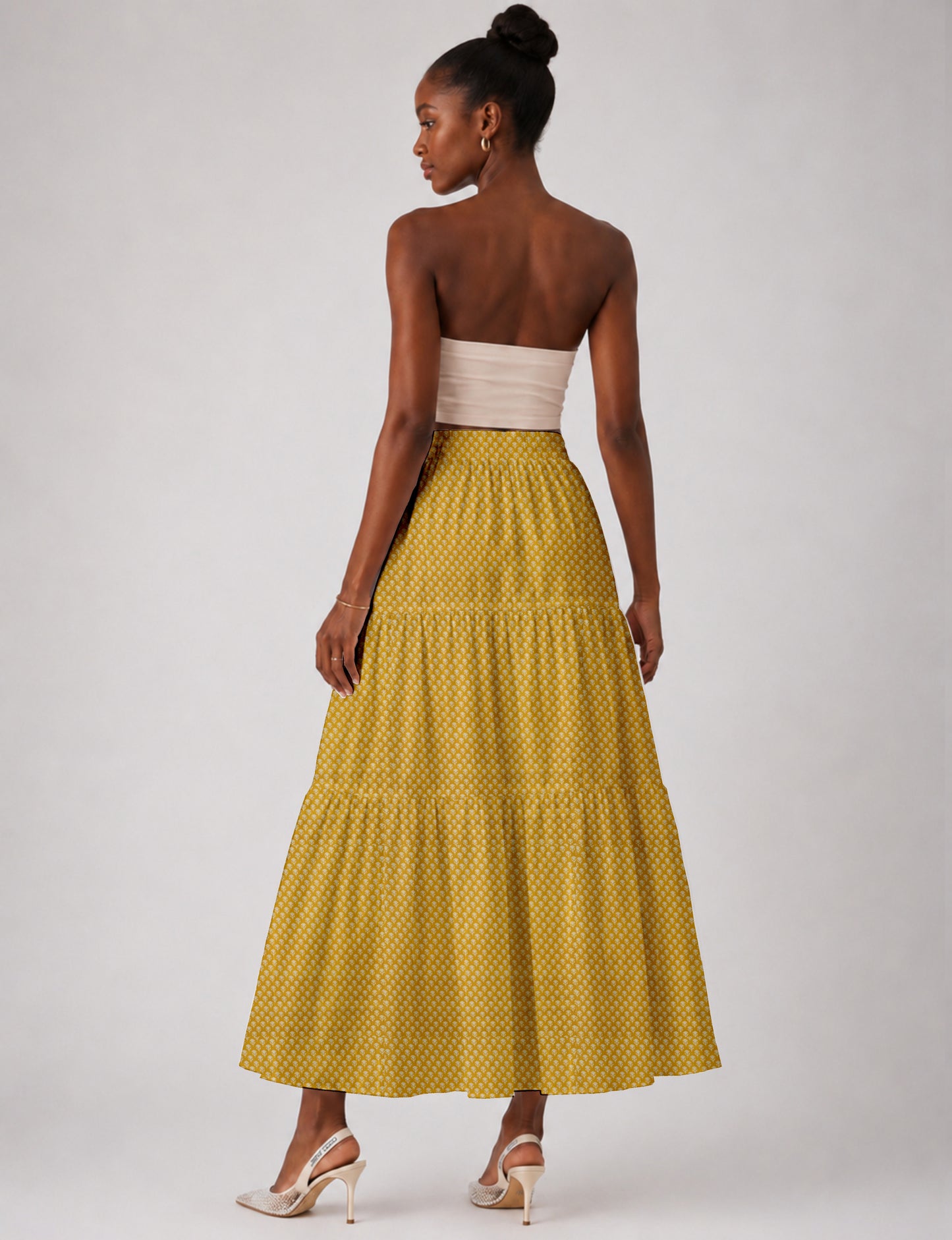 Woman wearing a yellow midi tiered skirt with a small geometric pattern, shown from the back, paired with beige top and
