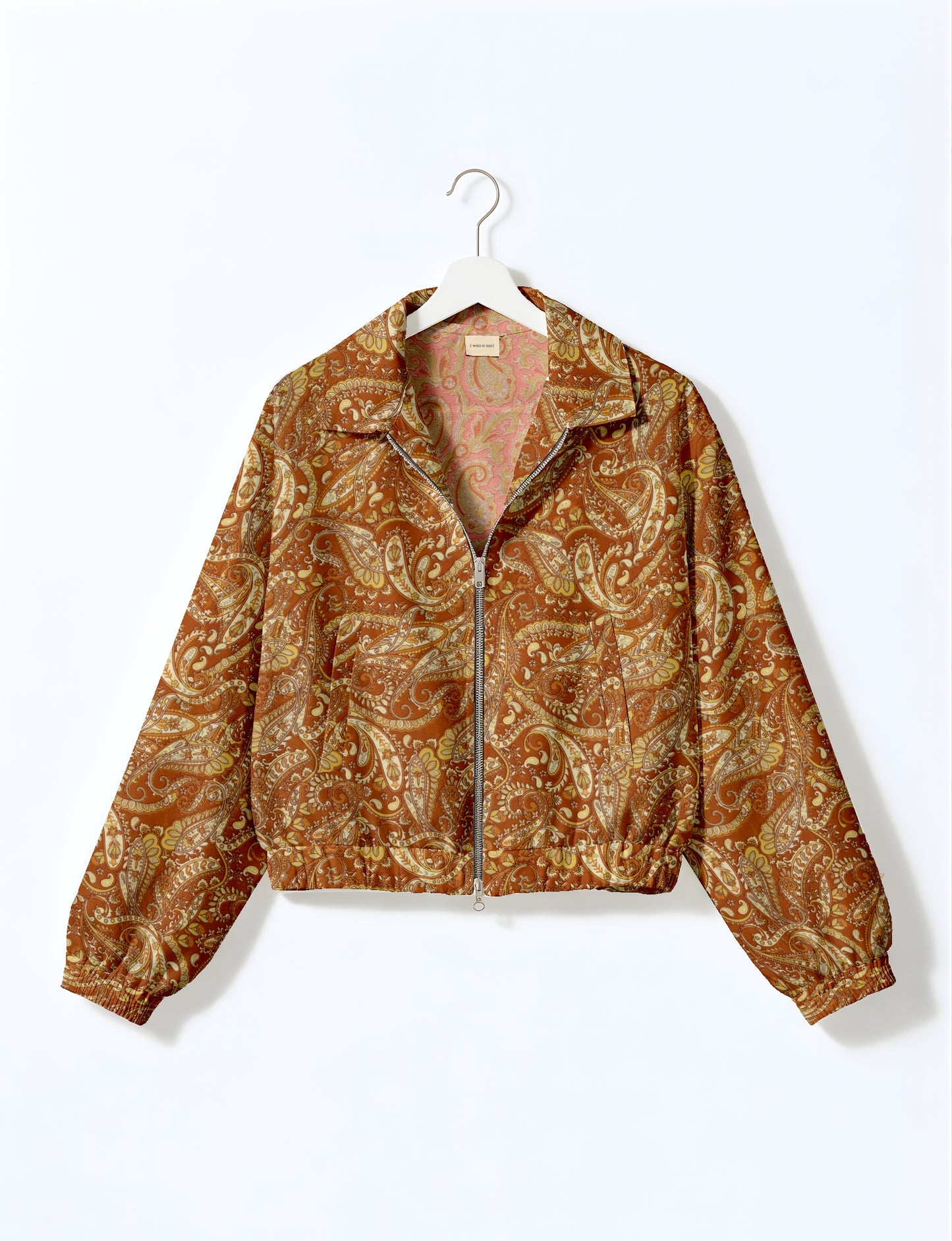 Brown paisley patterned bomber jacket with front zipper, elastic cuffs, and collar, hanging on white hanger against white
