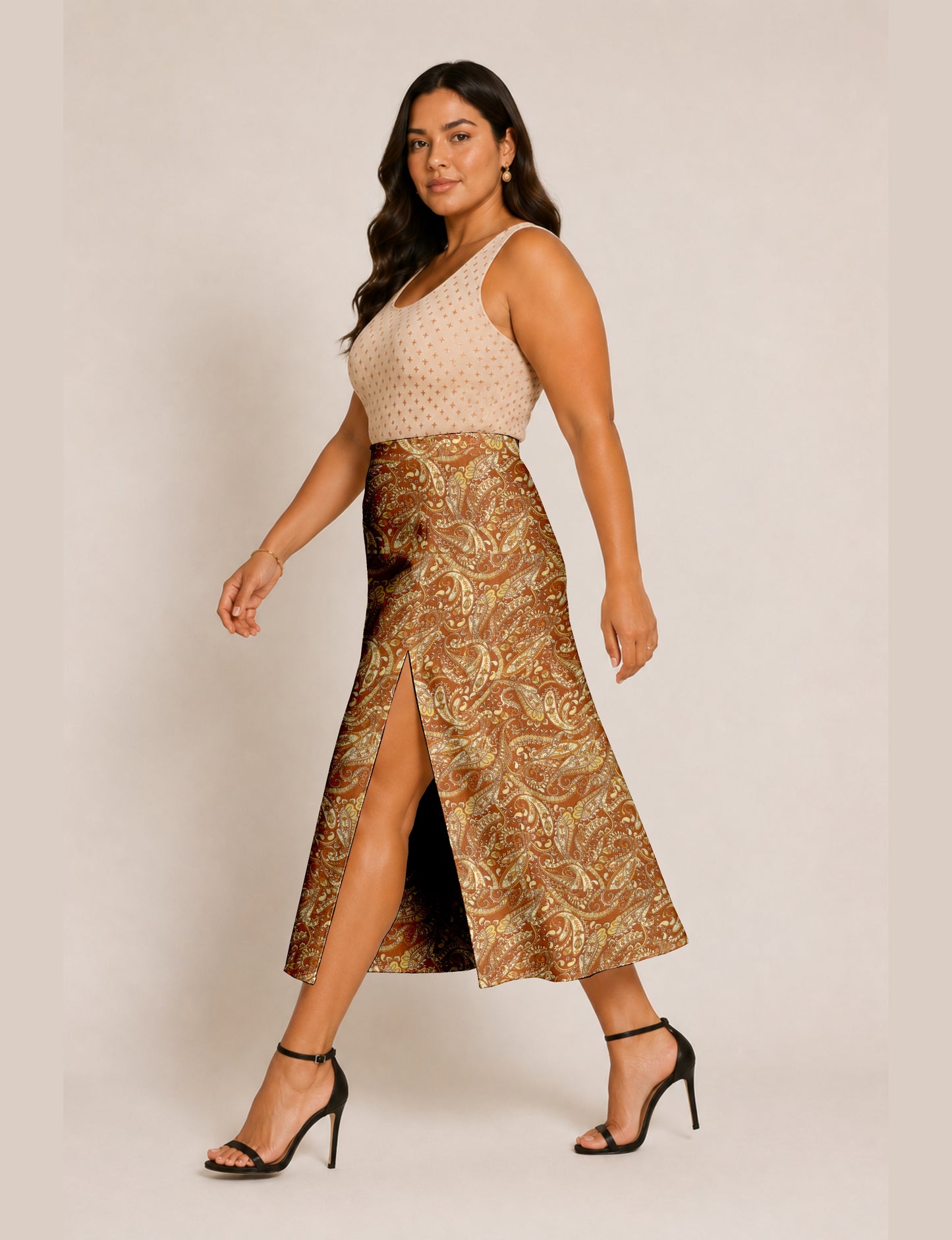Woman wearing a brown and yellow paisley A-line skirt with front slit, paired with a beige sleeveless top and black heels