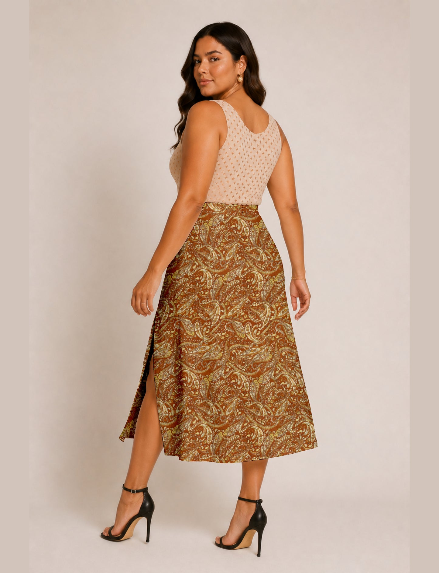 Woman wearing a brown and yellow paisley A-line skirt with side slit, paired with a sleeveless beige top with small cross