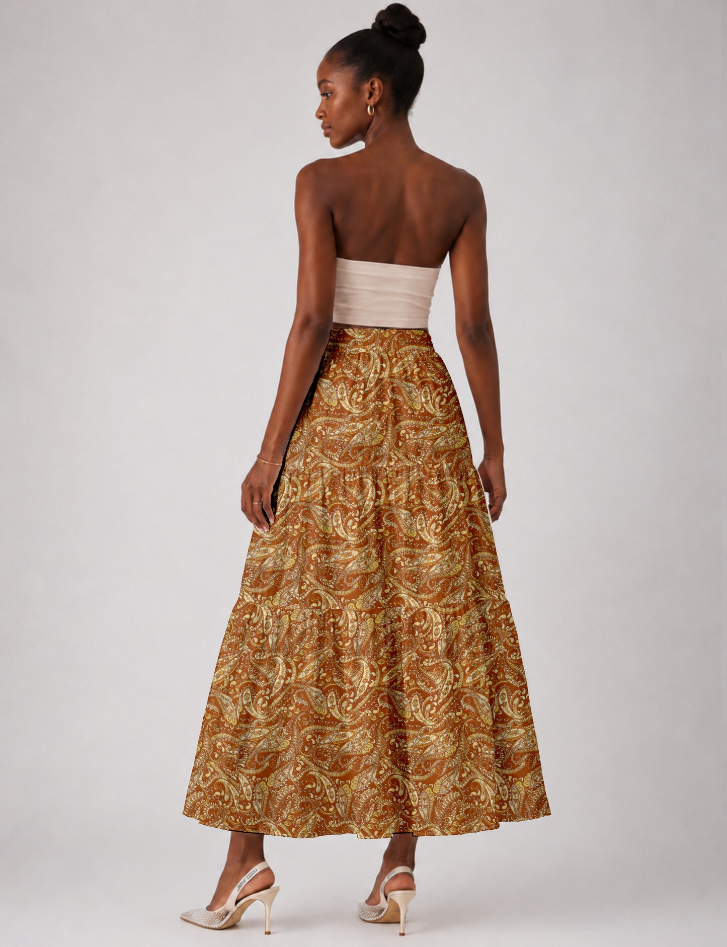 Woman wearing a yellow paisley midi tiered skirt, back view, paired with beige strapless top and beige high heels