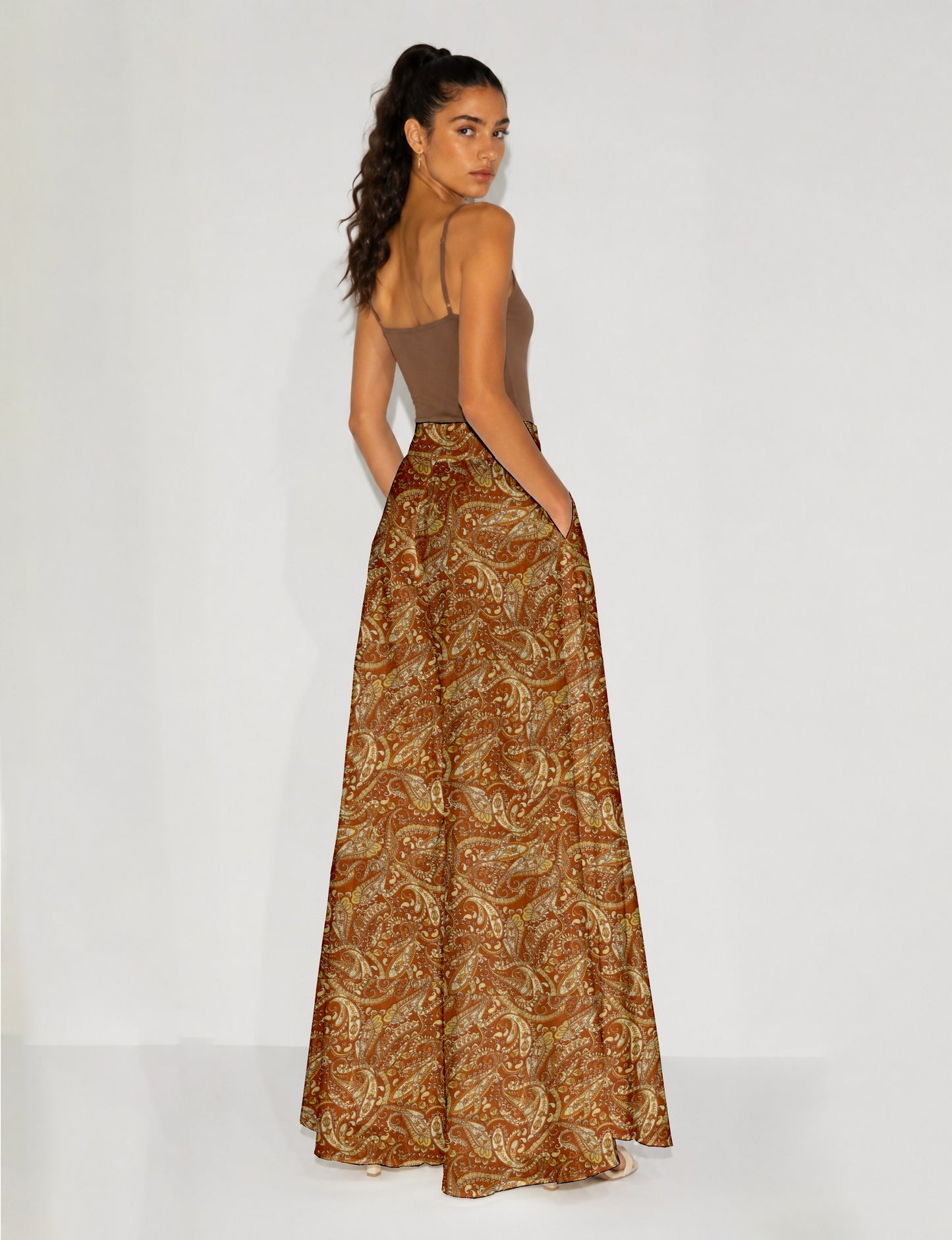 Woman wearing wide leg palazzo trousers with yellow paisley pattern, side pockets, paired with brown sleeveless top, back