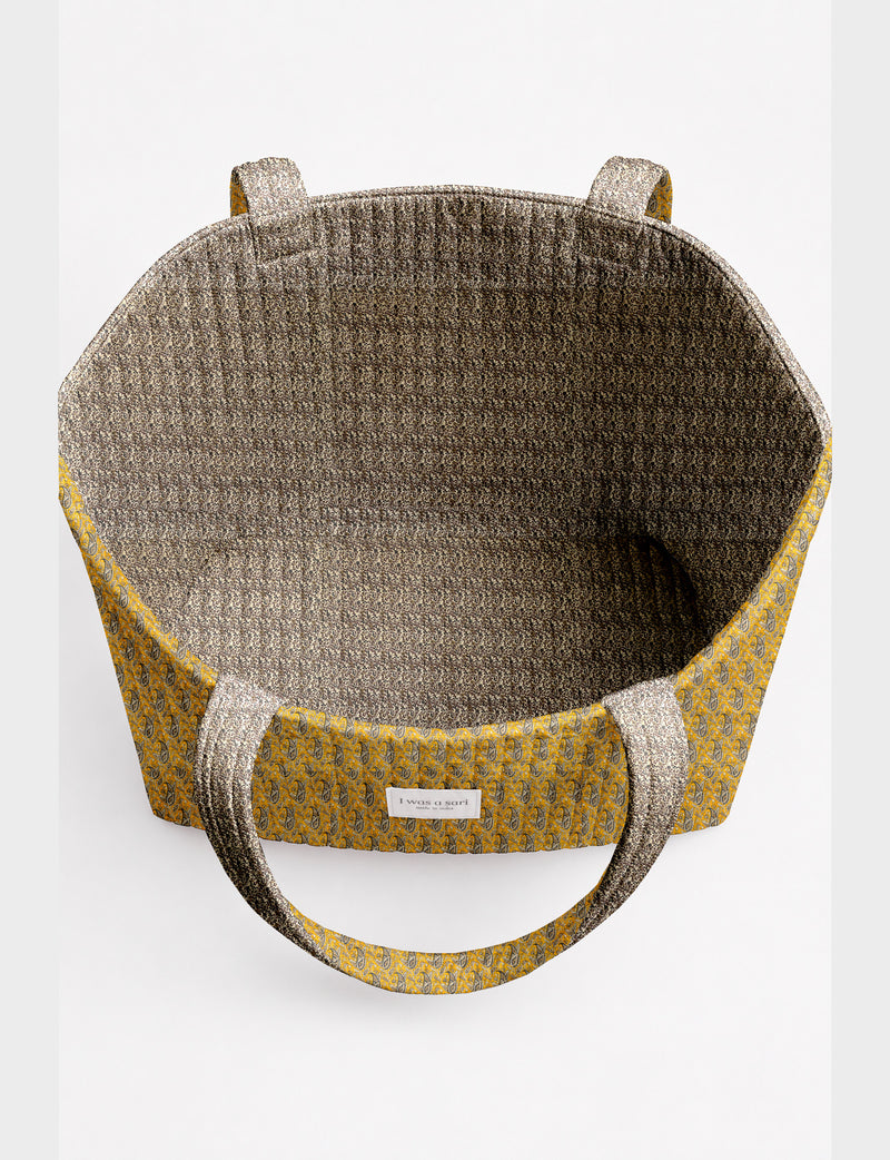 Quilted beach bag with yellow tropical exterior and red patterned interior, shown from top view with handles visible