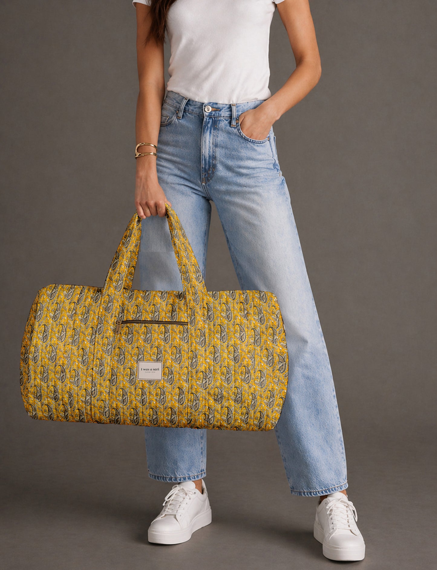 Quilted brown paisley barrel bag with double handles, front pocket, and gold zipper, shown in side angle view