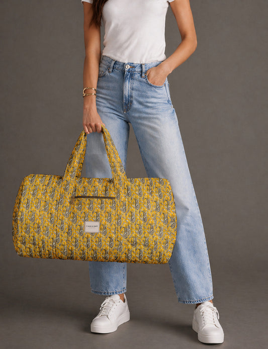 Quilted brown paisley barrel bag with double handles, front pocket, and gold zipper, shown in side angle view