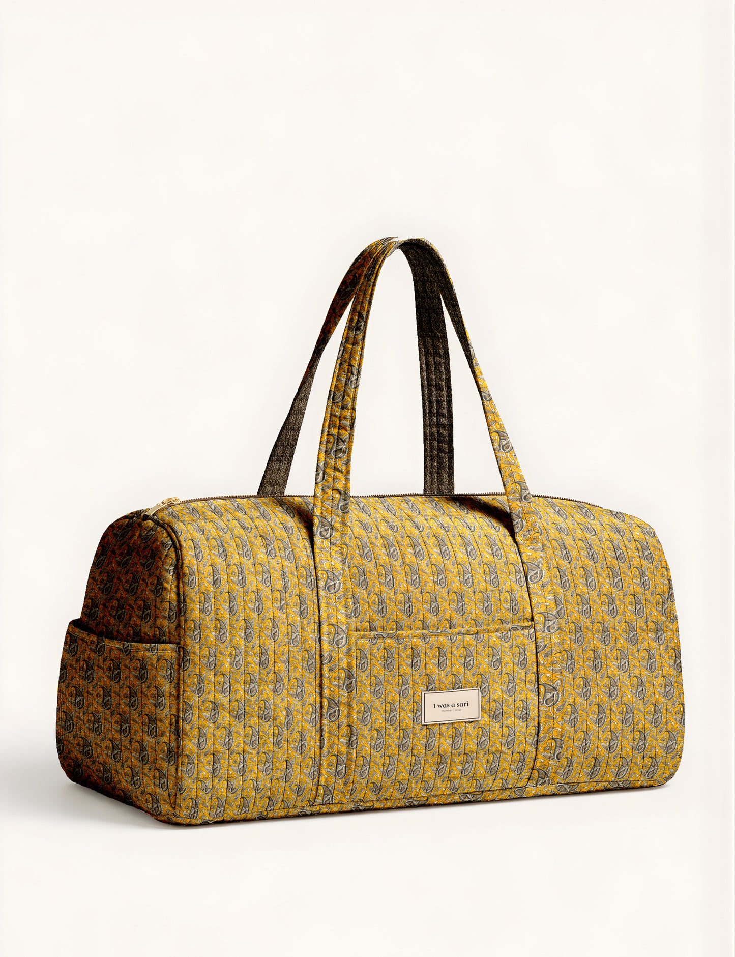 Woman holding a brown paisley quilted barrel bag with front zipper pocket, wearing light blue jeans and white sneakers
