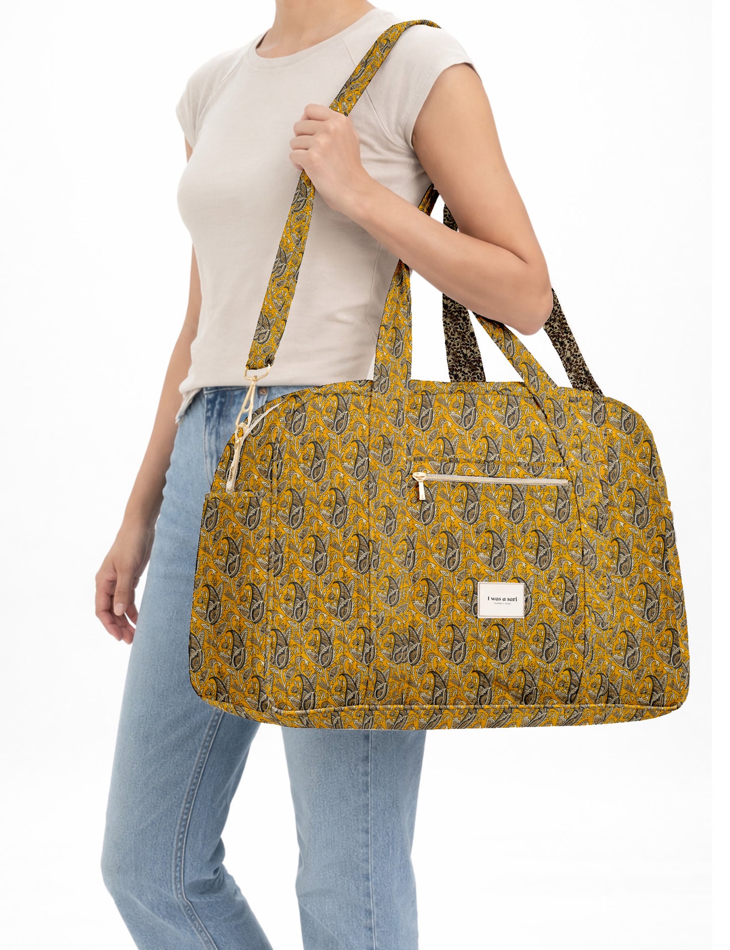 Brown quilted duffle bag with paisley pattern, front zip pocket, dual handles, and label reading "I was a sari"