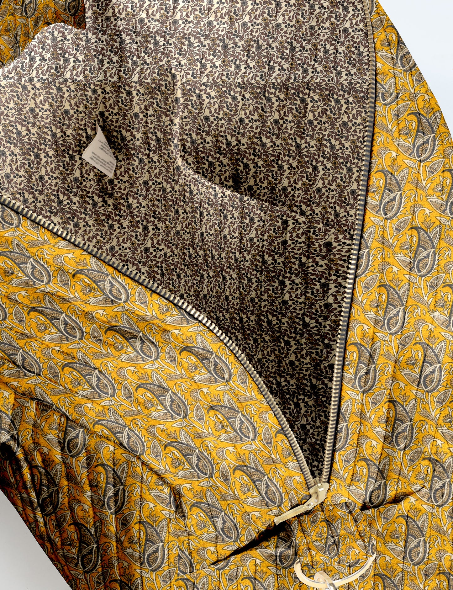 Brown quilted duffle bag with paisley pattern, front zip pocket, dual handles, and label reading "I was a sari"
