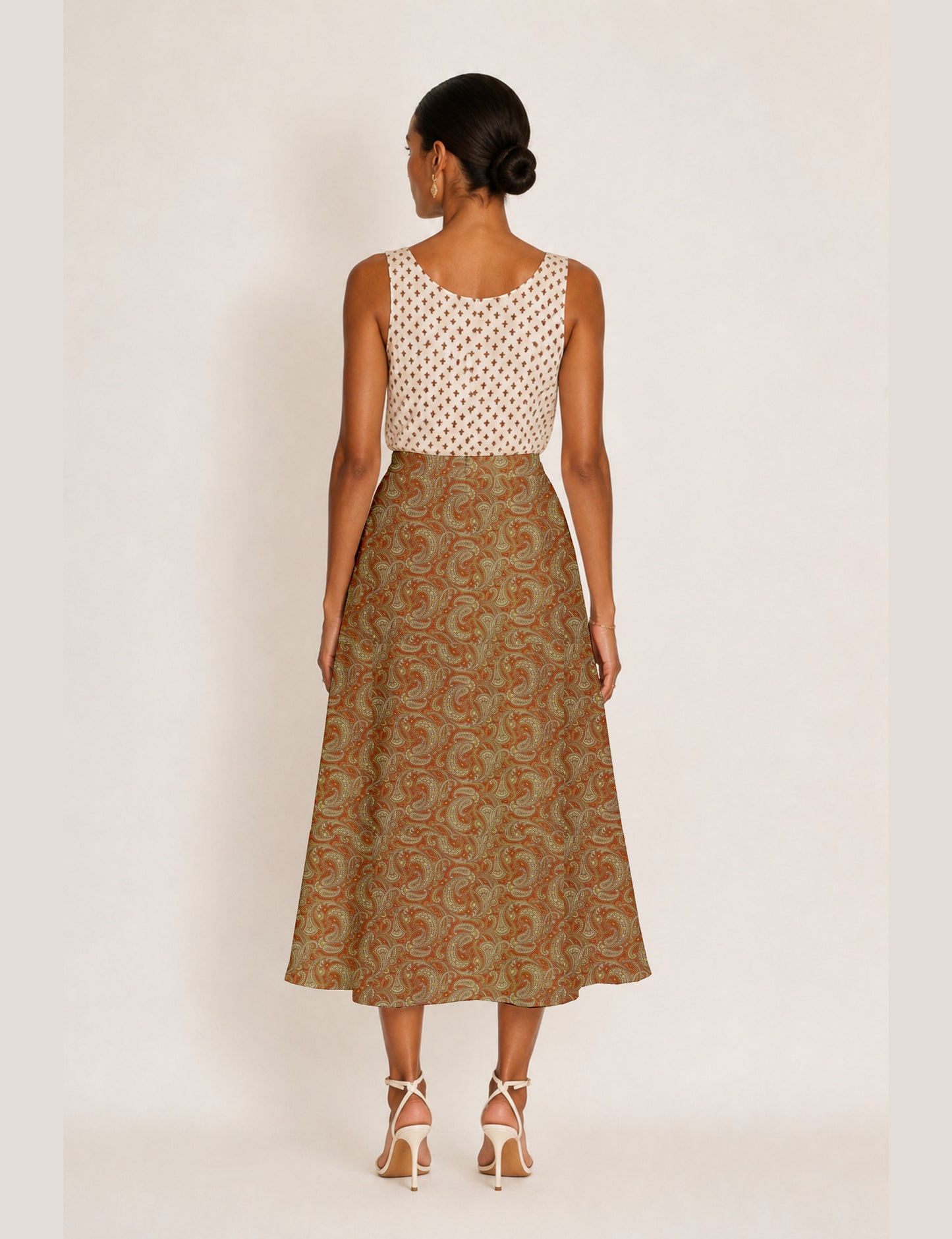 Woman wearing a yellow and black micro patterned A-line skirt with front slit, paired with beige sleeveless top and black