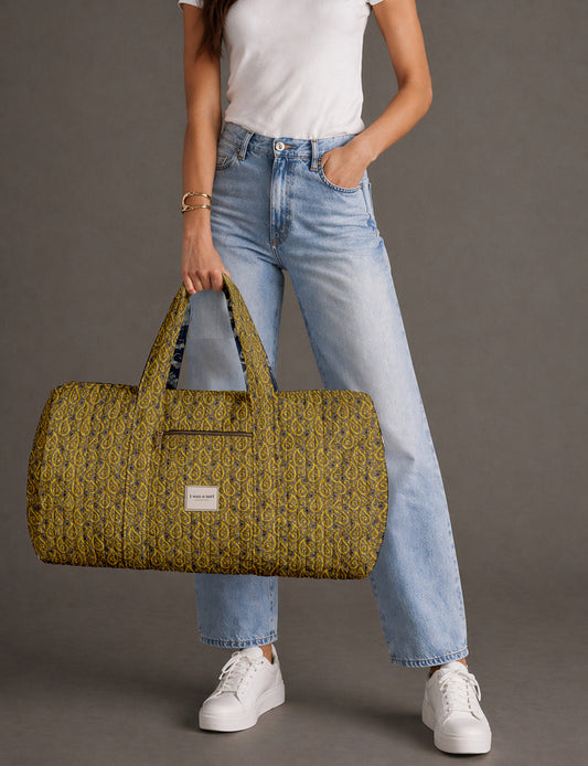 Quilted brown paisley barrel bag with double handles, front pocket, and gold zipper, shown in side angle view