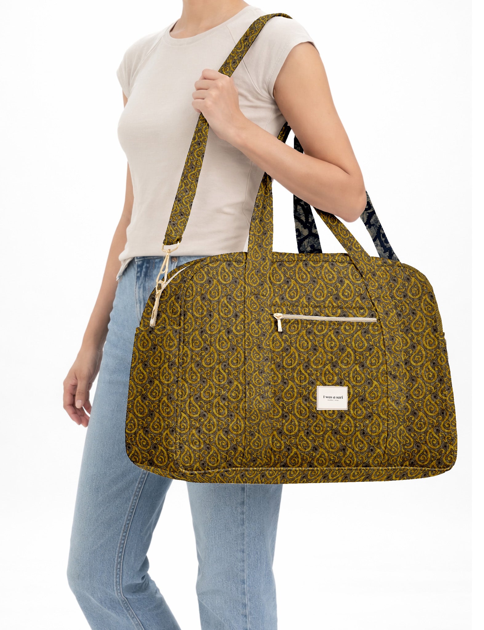 Brown quilted duffle bag with paisley pattern, front zip pocket, dual handles, and label reading "I was a sari"