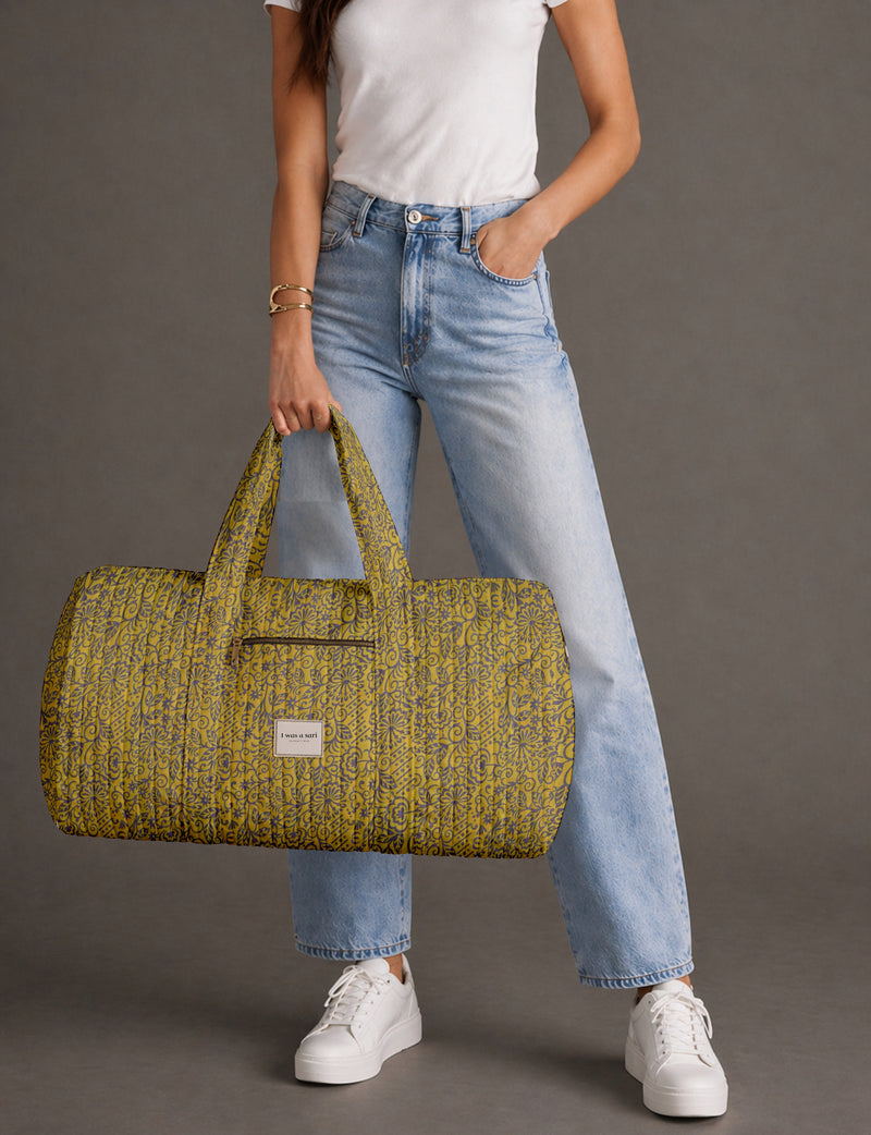 Woman wearing white t-shirt and light blue jeans holding a yellow quilted barrel bag with floral pattern and front zipper