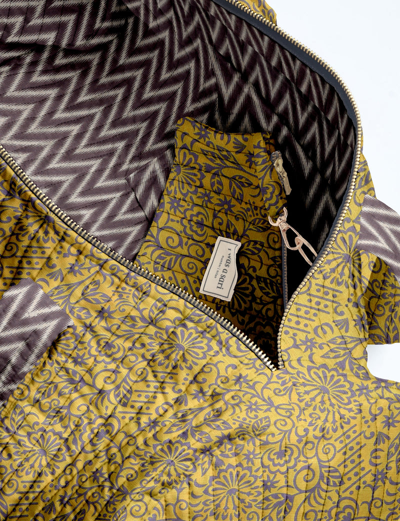 Quilted bowling bag with yellow floral exterior, purple zigzag interior lining, and gold zipper partially open showing label