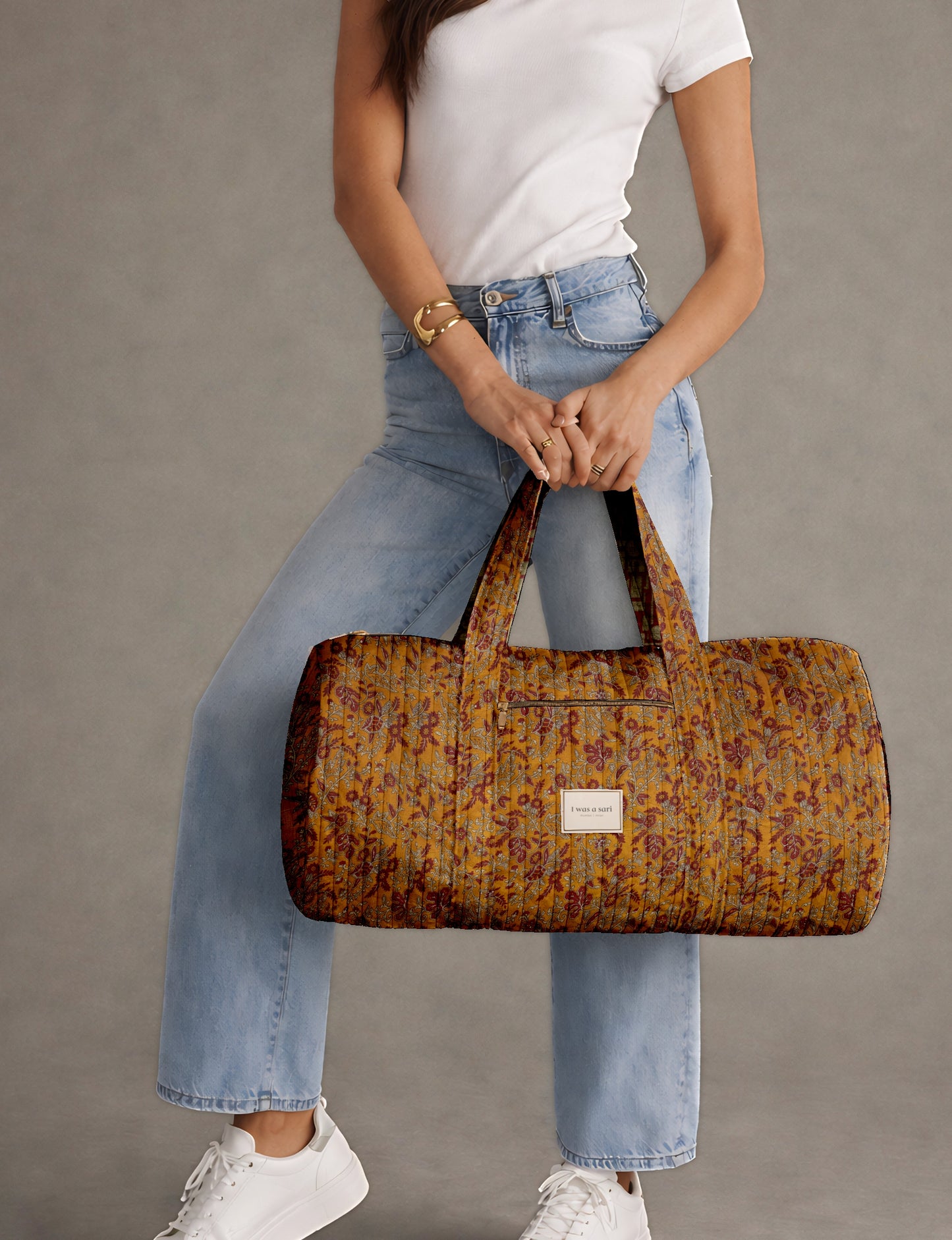 Woman wearing light blue jeans and white sneakers holding a beige quilted bowling bag with micro floral design and front