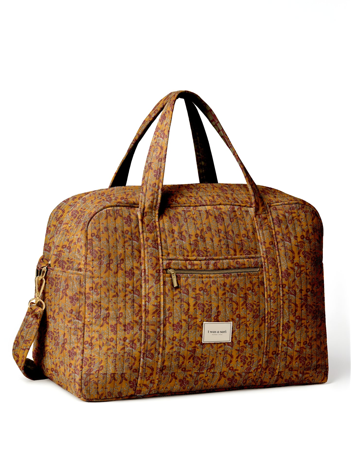 Quilted yellow tropical patterned duffle bag with dual handles, front zip pocket, and label reading "I was a sari"