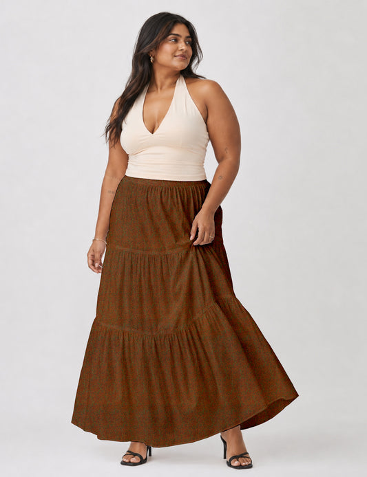 Woman wearing a yellow midi tiered skirt with a small geometric pattern, paired with a beige strapless top and white heels