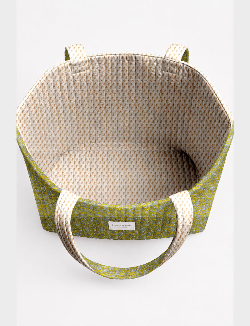 Quilted beach bag with yellow tropical exterior and red patterned interior, shown from top view with handles visible