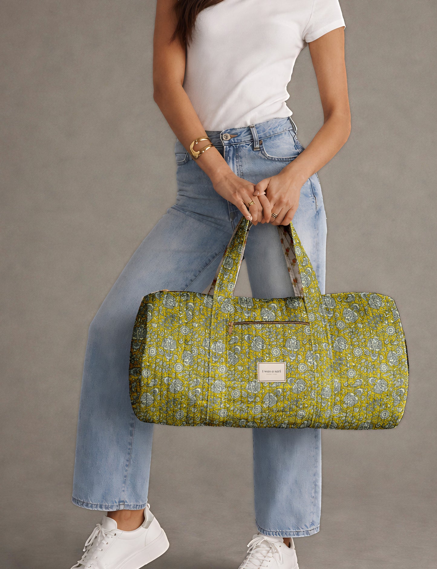 Brown paisley quilted bowling bag with front zipper pocket, held by person wearing white shirt and light blue jeans