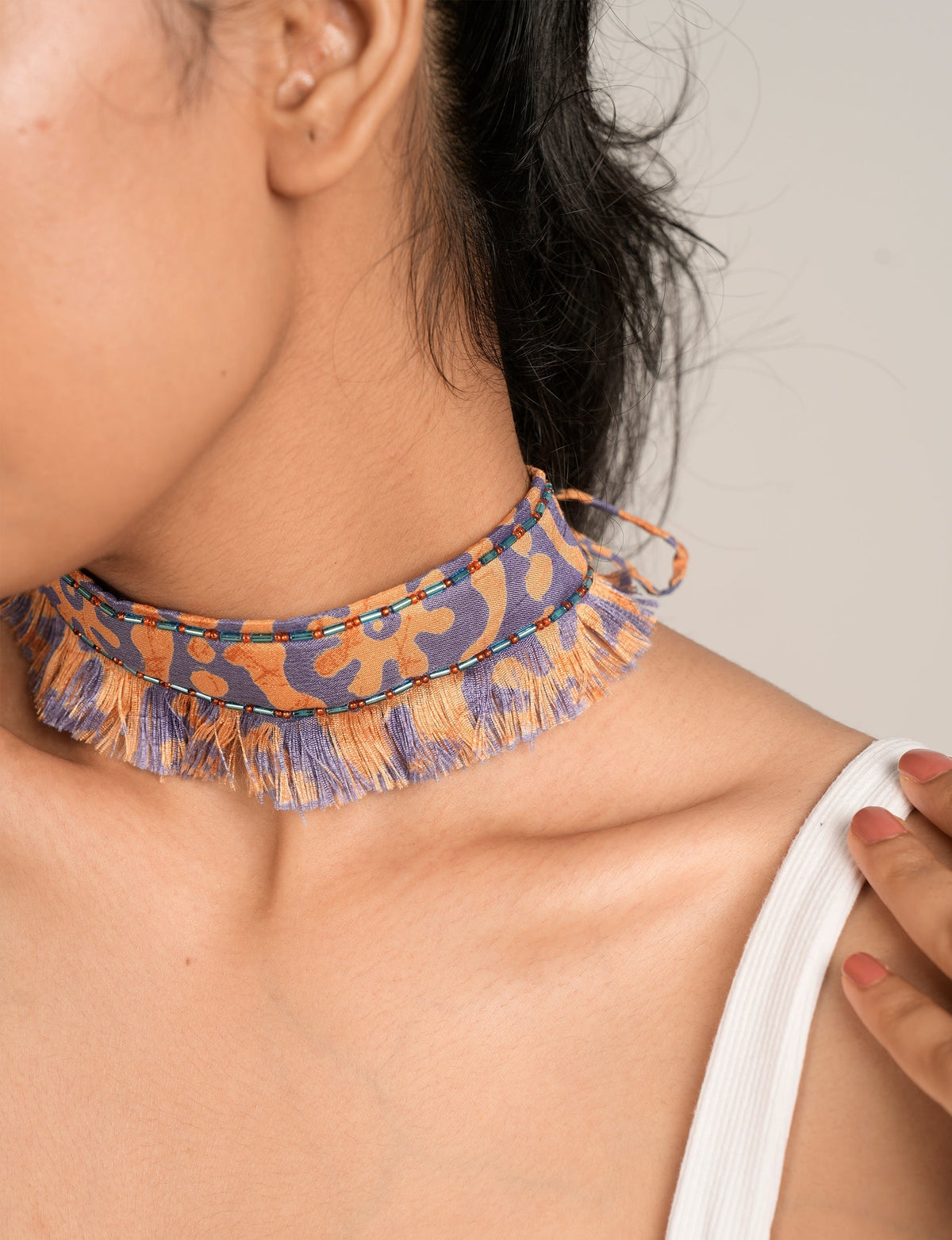 Red and purple abstract patterned fabric choker with fringe and blue and orange bead detailing, worn by model side view