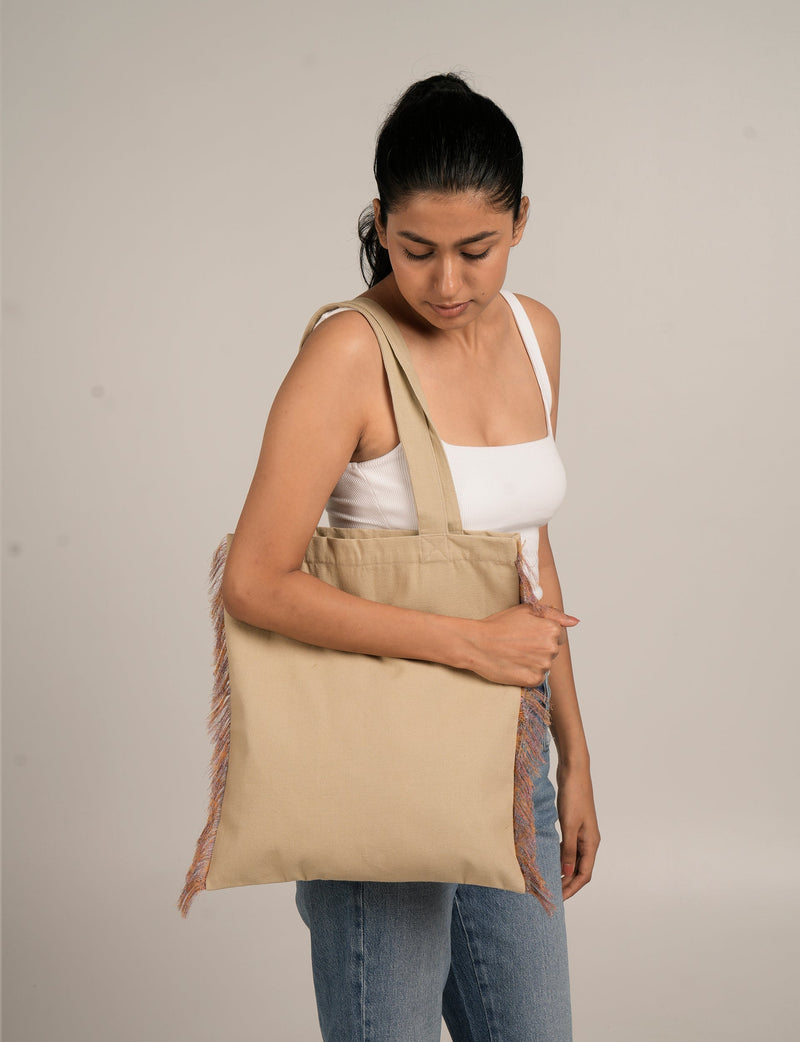 Woman wearing a beige canvas tote bag with multicolor fringe details on sides, shown from front and side angles