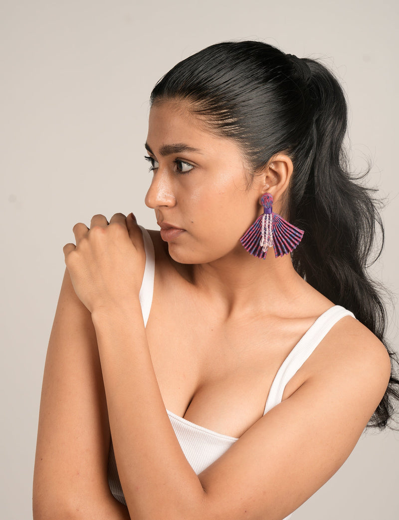 Model wearing pink and purple pleated fabric earrings with clear bead tassels, side view, against plain background