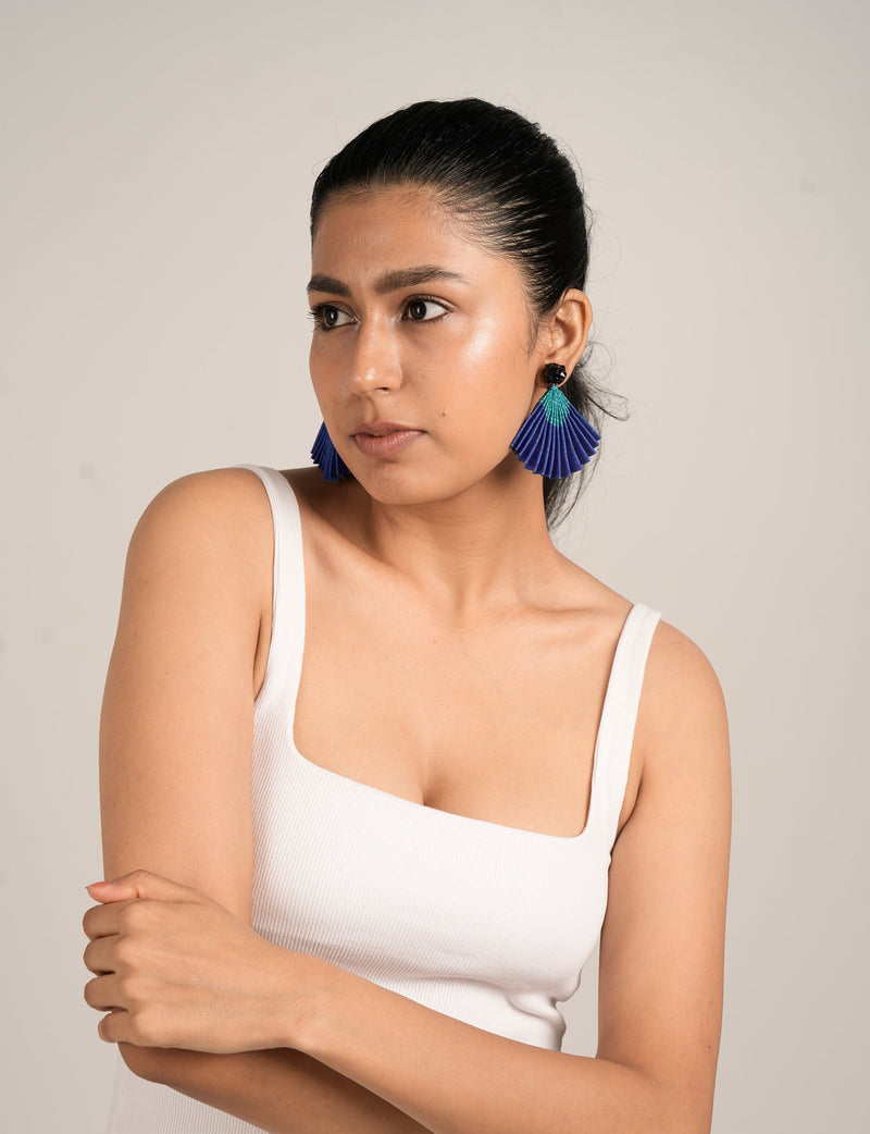 Model wearing pleated fan-shaped earrings in blue and teal with black stud, shown from front side angle in white tank top