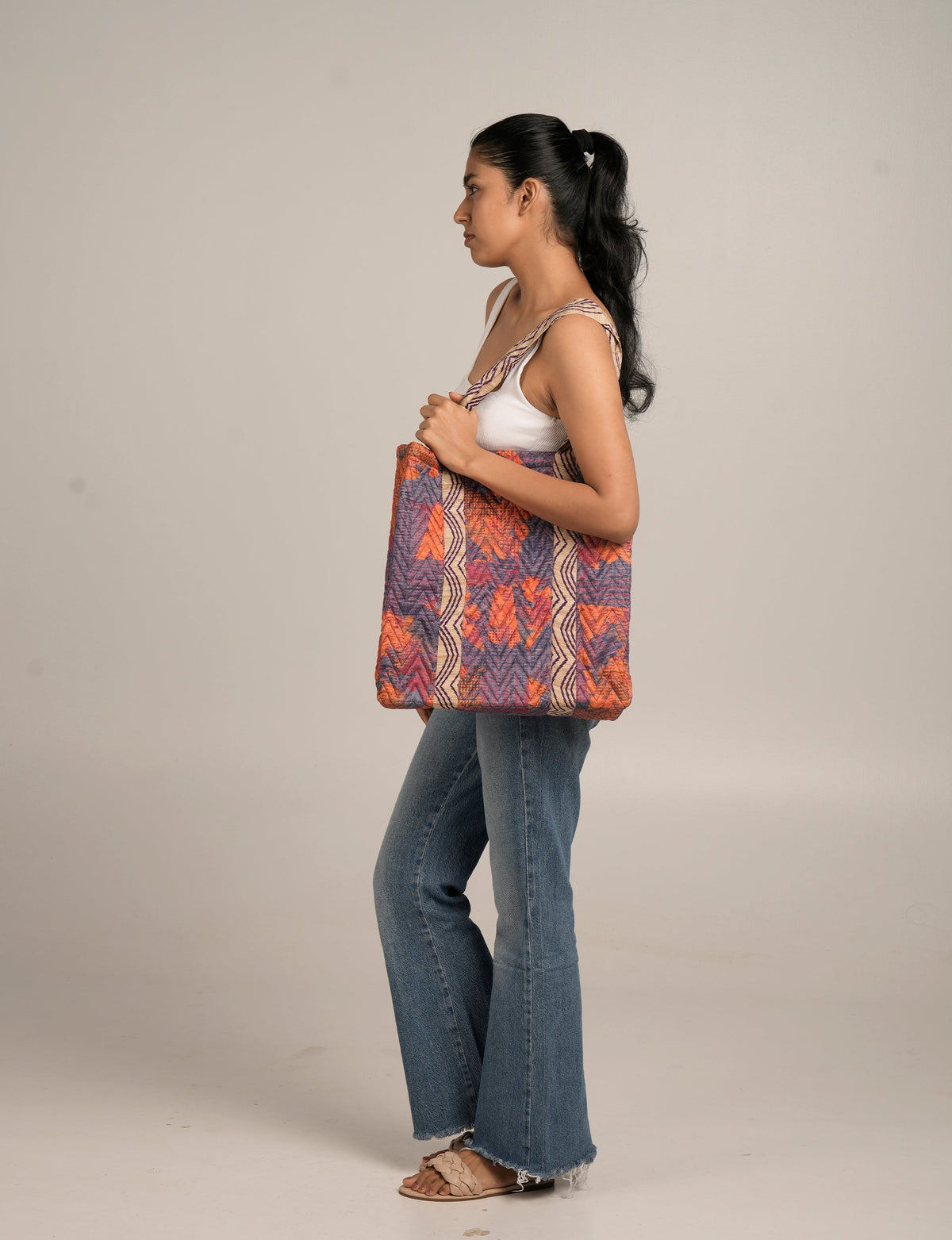 Woman wearing a quilted tote bag with orange, purple, and beige abstract patterns over her shoulder, side view