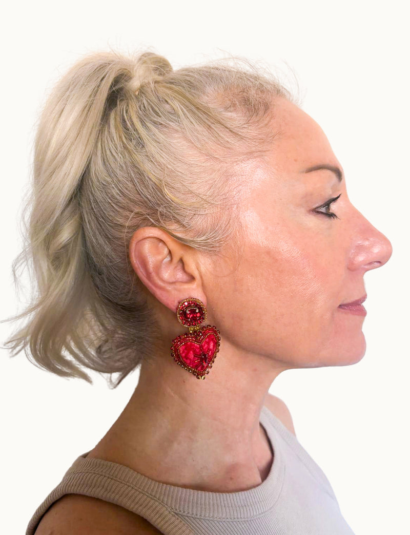 Woman wearing pink abstract heart drop earrings with beaded details, shown in close-up side profile view
