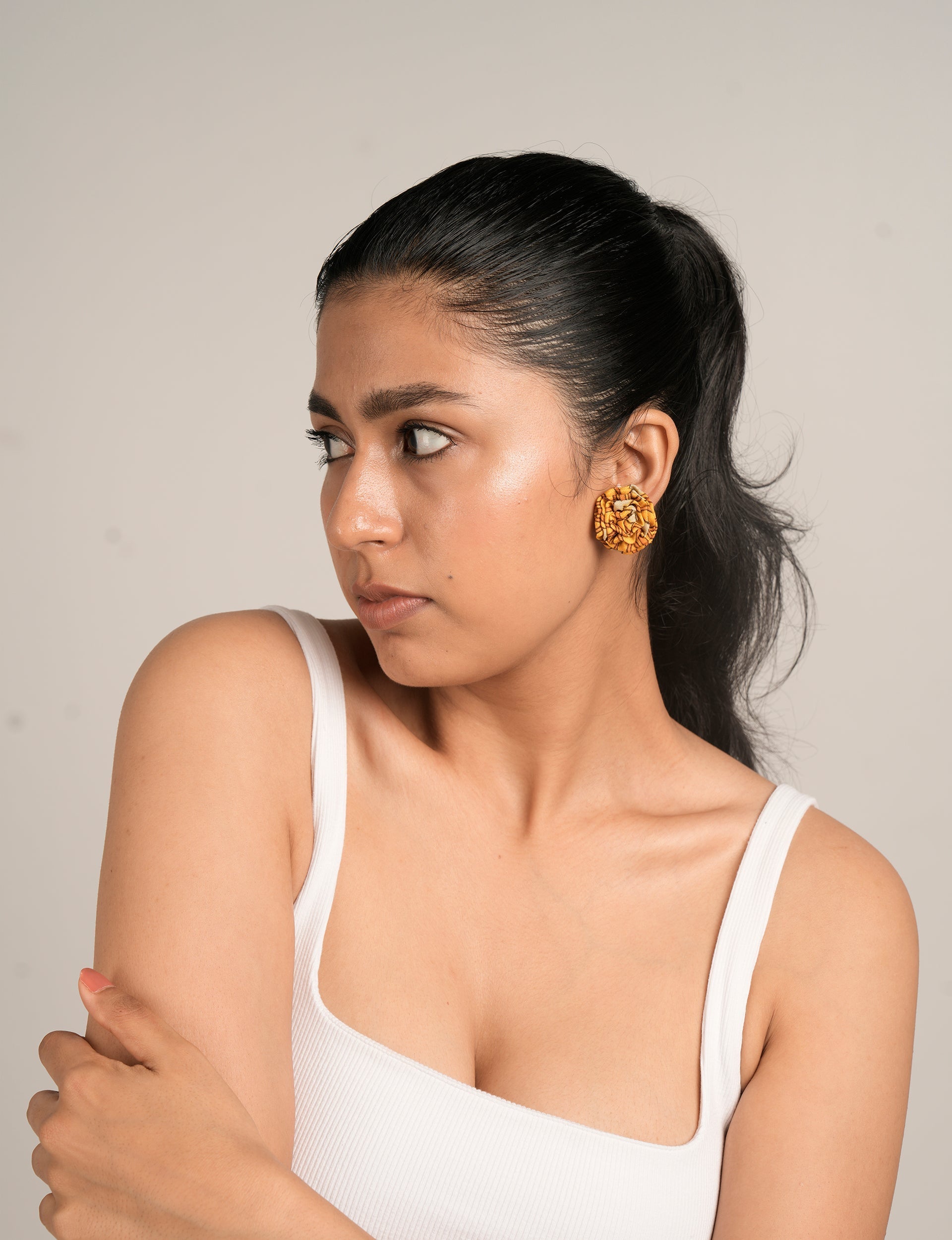Woman wearing yellow-orange ruffle earrings with a white sleeveless ribbed top, side view on neutral background