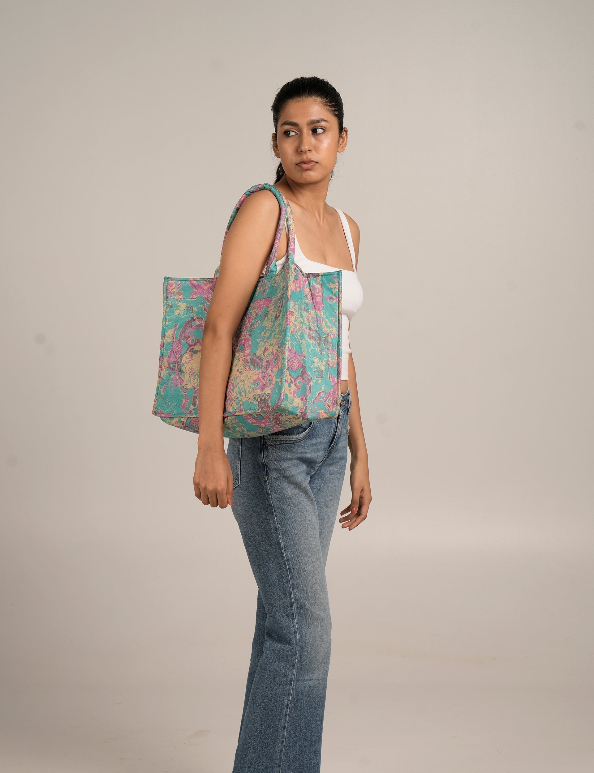 Woman wearing a blue tropical patterned work tote bag with padded handles over her shoulder, side view on plain background