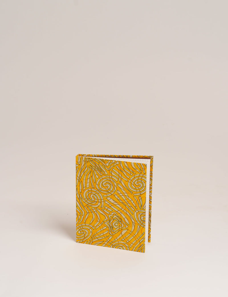 A6 hard cover notebook with yellow abstract swirl and line pattern, standing upright on a plain background