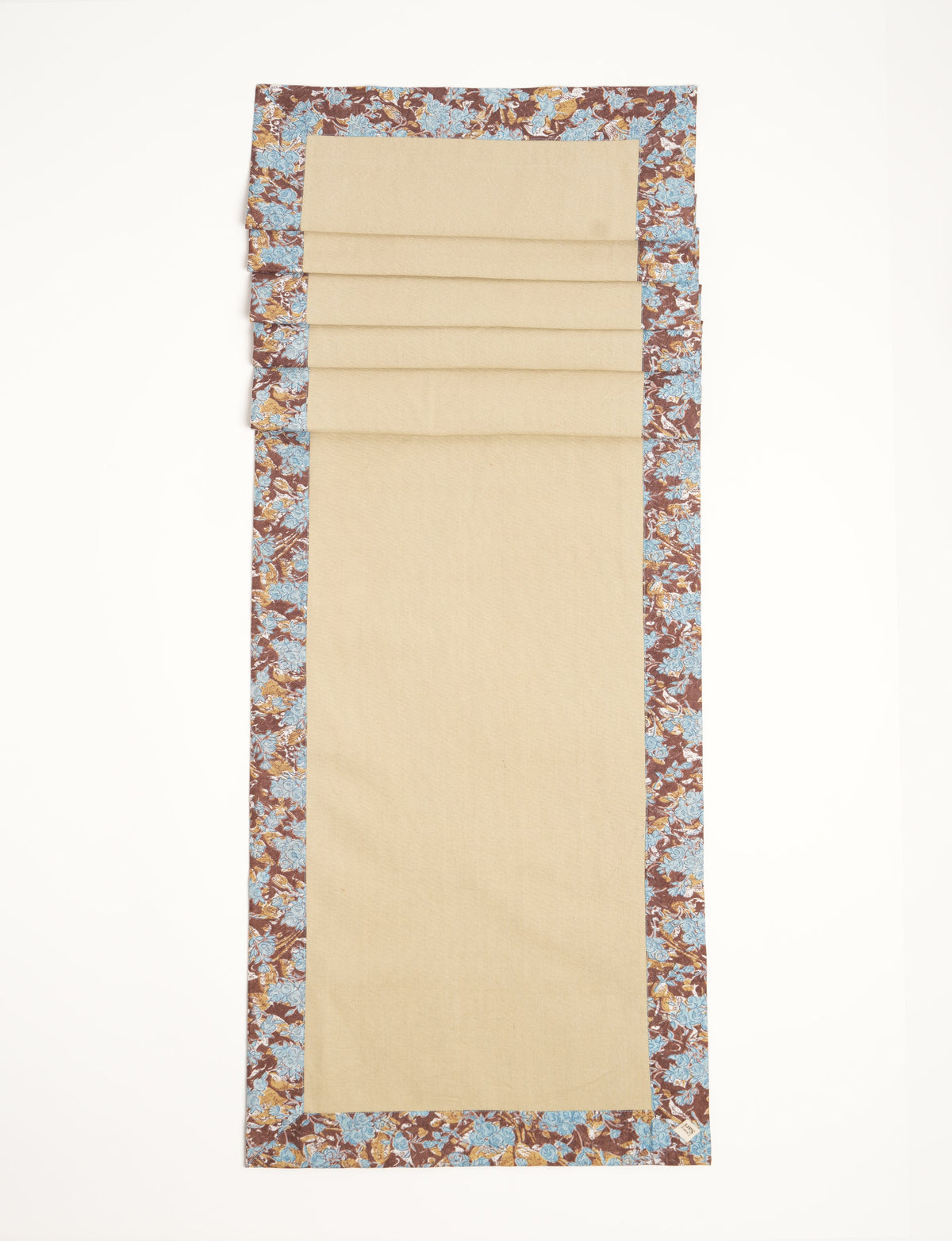 Brown table runner with blue floral border and beige center, flat laid with visible fabric texture and corner label