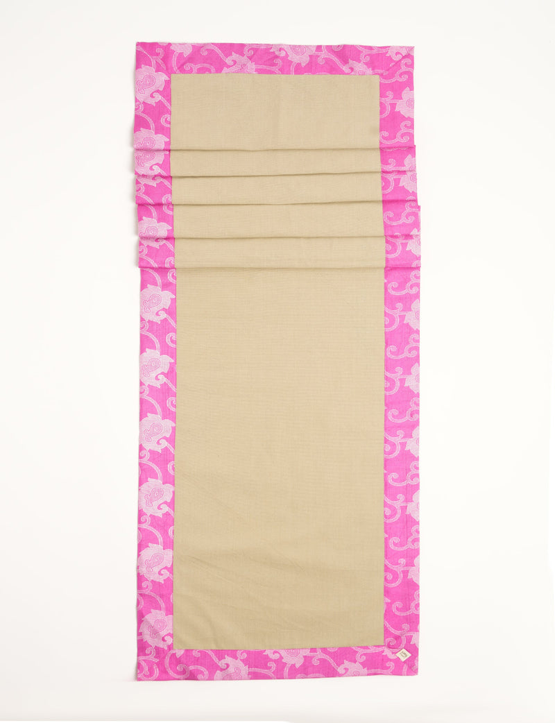 Rectangular beige table runner with bright pink ethnic floral border, shown flat with visible fabric texture and tag