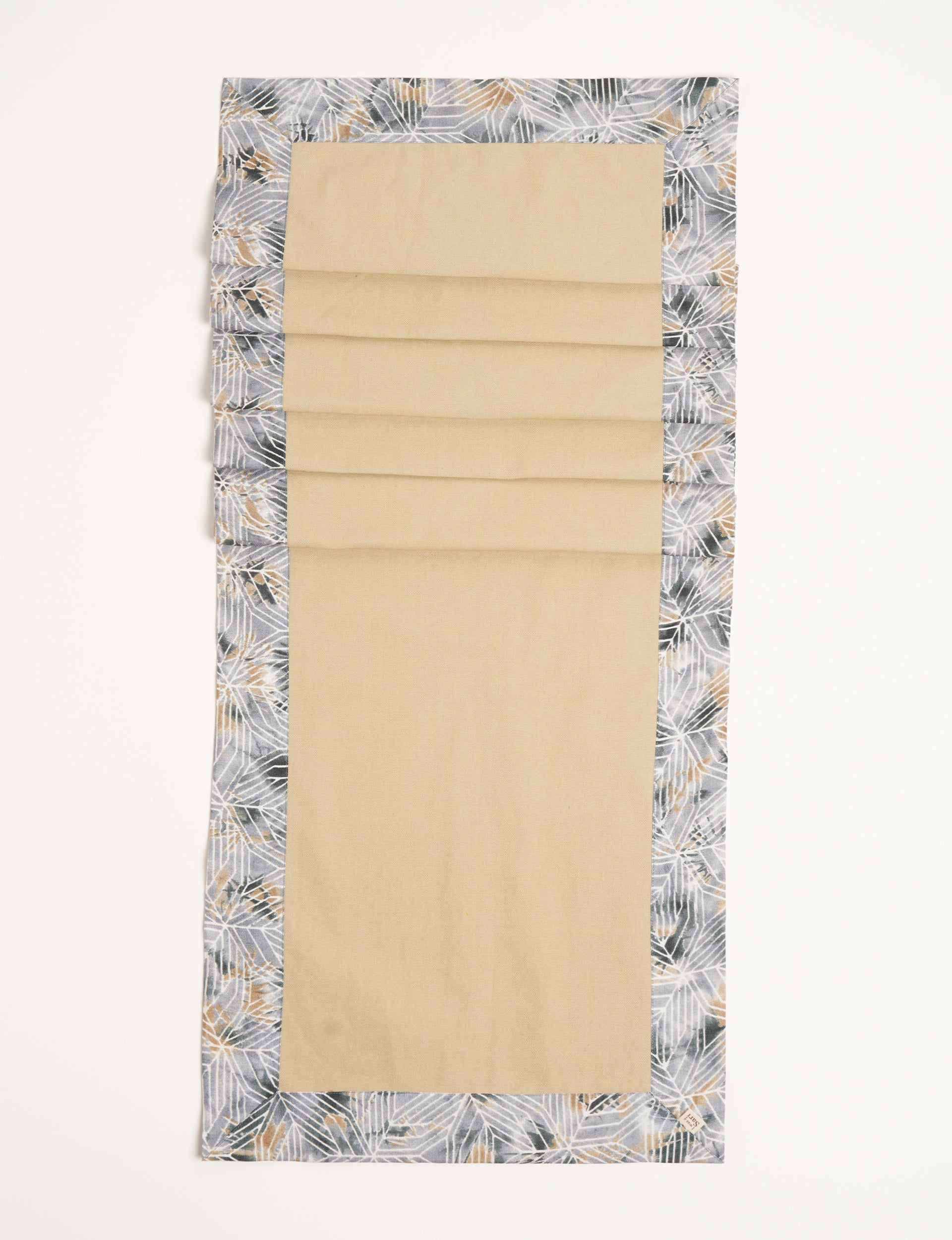 Beige table runner with grey geometric patterned border and small fabric tag on corner, flat lay view